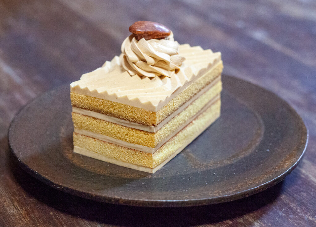 A rectangular slice of what appears to be some kind of coffee sponge cake with a coffee bean on top. There are three layers with a layer of coffee cream in between.