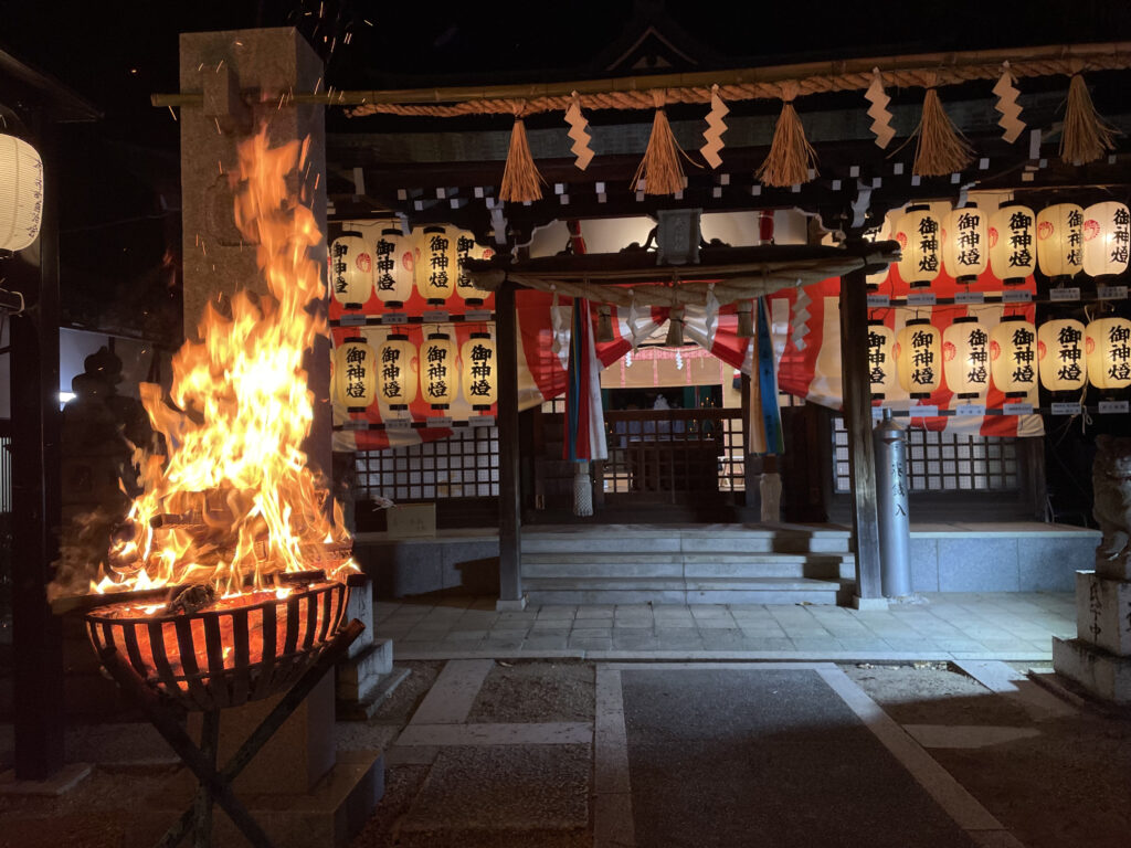 A Japanese shrine at night with a fire blazing to the left.